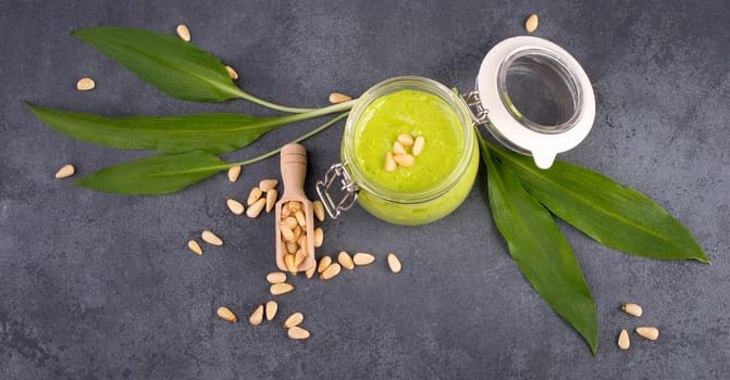 Pesto made from wild garlic, pine nuts and feta cheese in a glass, with fresh leaves on a dark textured background, empty space for text