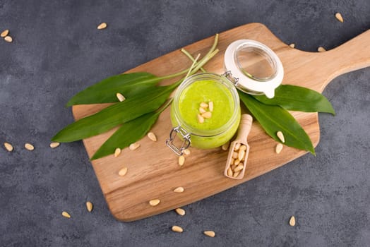 Pesto made from wild garlic, pine nuts and feta cheese in a glass, with fresh leaves on a dark textured background, empty space for text