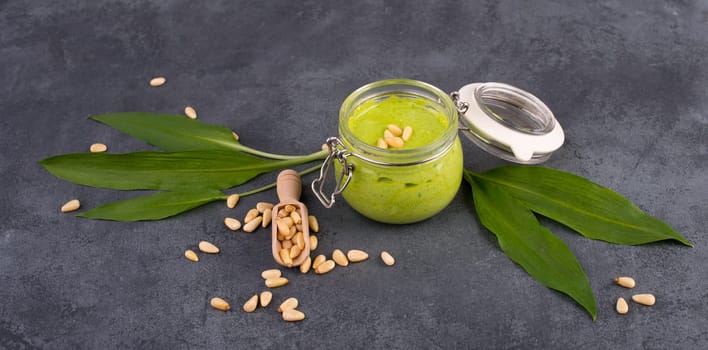 Pesto made from wild garlic, pine nuts and feta cheese in a glass, with fresh leaves on a dark textured background, empty space for text