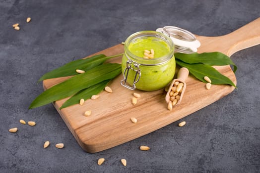 Pesto made from wild garlic, pine nuts and feta cheese in a glass, with fresh leaves on a dark textured background, empty space for text