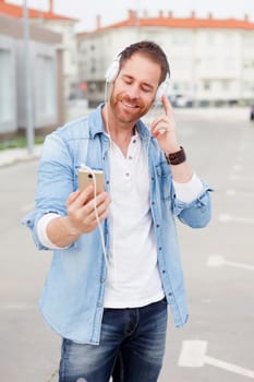 Casual guy next to a vintage bicycle listening music with headphones wearing denim shirt