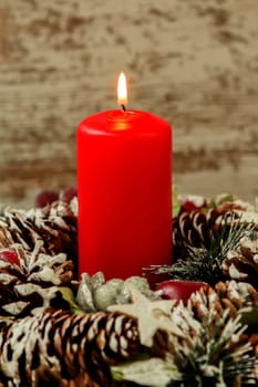 Red candle lit and pinecones for Christmas on a wooden background