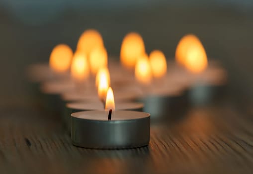 Many small burning candles on a wooden surface