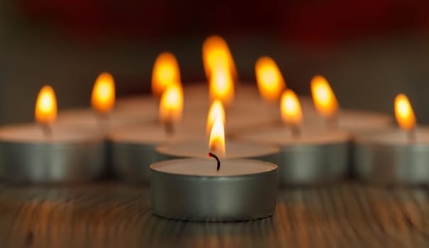 Many small burning candles on a wooden surface