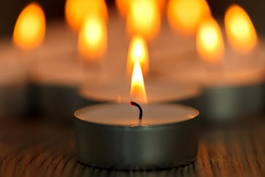 Many small burning candles on a wooden surface