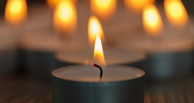 Many small burning candles on a wooden surface