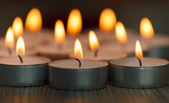 Many small burning candles on a wooden surface