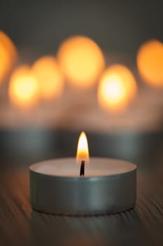 Many small burning candles on a wooden surface