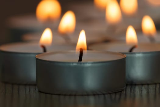 Many small burning candles on a wooden surface