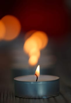 Many small burning candles on a wooden surface