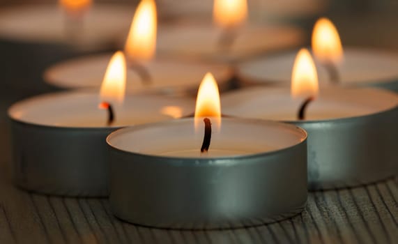 Many small burning candles on a wooden surface