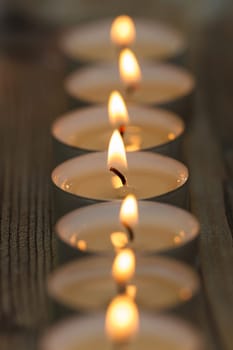 Many small burning candles in line on a wooden surface