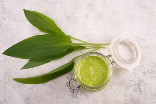 Pesto made from wild garlic, pine nuts and feta cheese in a glass, with fresh leaves on a textured background, empty space for text