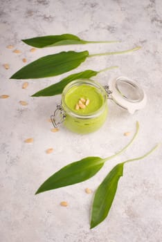 Pesto made from wild garlic, pine nuts and feta cheese in a glass, with fresh leaves on a textured background, empty space for text