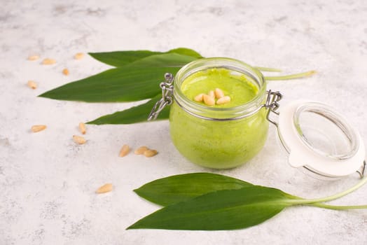 Pesto made from wild garlic, pine nuts and feta cheese in a glass, with fresh leaves on a textured background, empty space for text