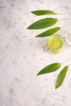 Pesto made from wild garlic, pine nuts and feta cheese in a glass, with fresh leaves on a textured background, empty space for text