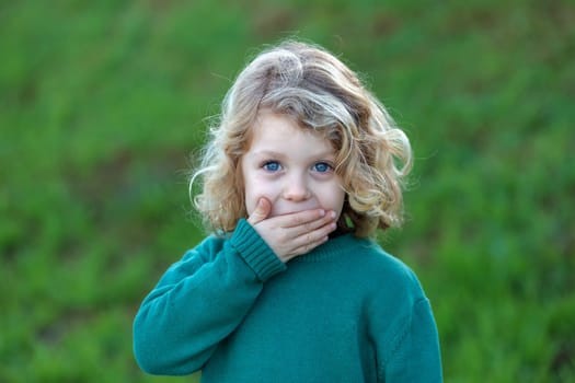 Surprised blond child with blue eyes covering his mouth