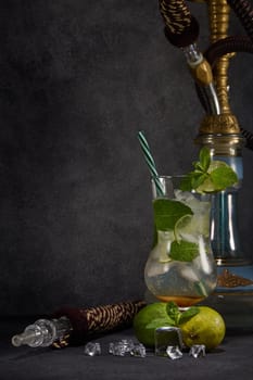 Hookah (shisha) and glass of Mojito cocktail with lime and ice on dark grey background with copy space. Weekend or holiday party. Hookah bar, nightclub
