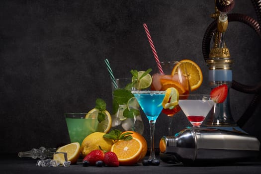 Hookah and cocktails set. Glasses with various cold  beverages, fruits, shisha and bar tool on dark grey background with copy space. Weekend or holiday party. Hookah bar, cocktail bar.