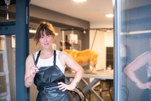 portrait of professional pet hairdresser hipster woman with tattoos while standing at the door of her beauty salon for animals