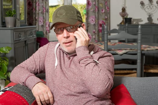 a senior with a phone sitting on the sofa in his house