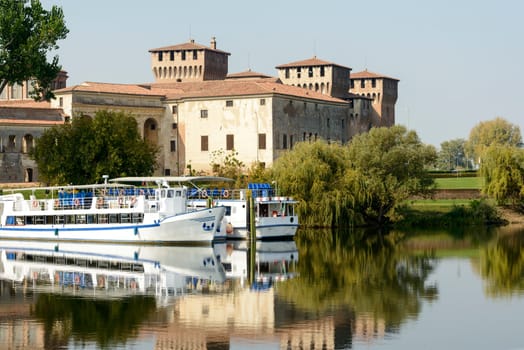 view of touristic passenger vessels and east side of Gonzaga Ducale Palace in background, shot in bright autumn sun light  at Mantua, Lombardy, Italy.