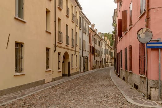 view of old houses on bending cobbled street in city center, shot in bright cloudy light  at Mantua, Lombardy, Italy.