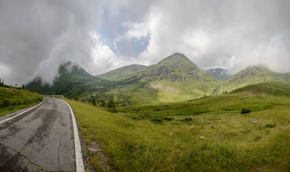 Vivione pass narrow mountain road crosses high altitude meadows,  shot in cloudy summer light in Scalve valley, Bergamo, Orobie, Lombardy, Italy .