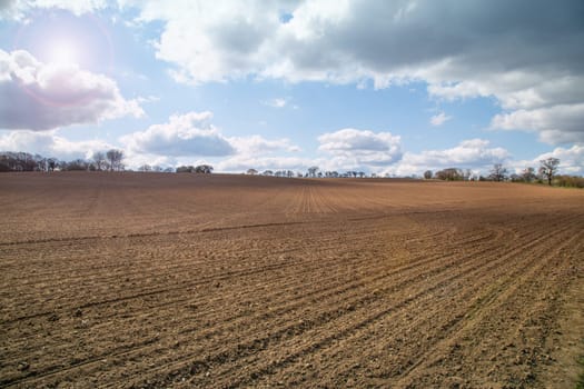 Plowed agricultural spring field during sunny day, dramatic sky, soil texture close up. Rural scene. Farm and food industry. Furrows row pattern in a plowed field in spring. Horizontal perspective