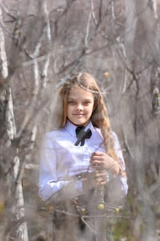 A girl in medieval style clothes stands with a sword, in the foreground and background blurred branches of bushes in the forest