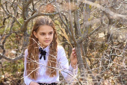 A girl in a white shirt and a bow tie around her neck walks through the spring forest, close-up portrait