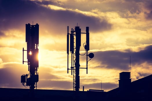 Silhouette of communication or cell tower on the rooftop of a building, evening sunshine