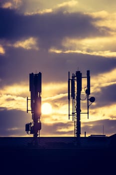 Silhouette of communication or cell tower on the rooftop of a building, evening sunshine