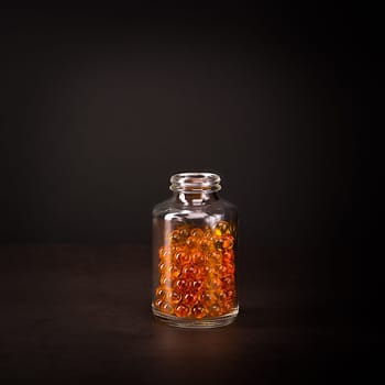 A glass jar with pills of bright orange yellow color on a brown background. Place for the label, logo, layout.