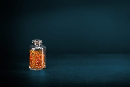 A glass jar with pills of bright orange yellow color on a blue background. Place for the label, logo, layout.