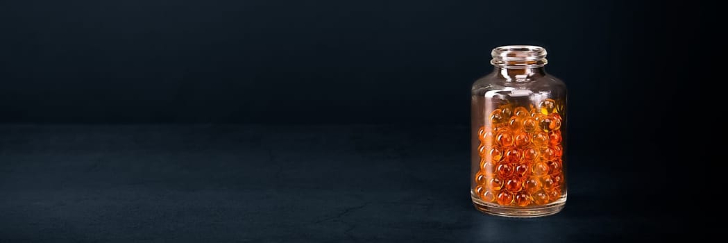 A glass jar with pills of bright orange yellow color on a blue background. Place for the label, logo, layout.