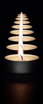 A row of burning candles on a dark background with a flare in the foreground. Layout, mockup.