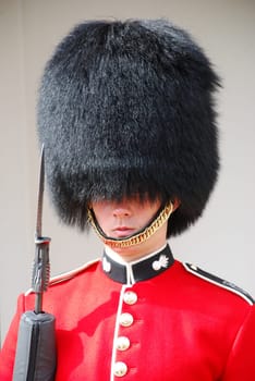 Grenadiers of the Coldstream Guard guard Buckingham Palace and the Tower of London with a rifle. They wear the famous bearskin hat. A soldier stands at the Jewel House.