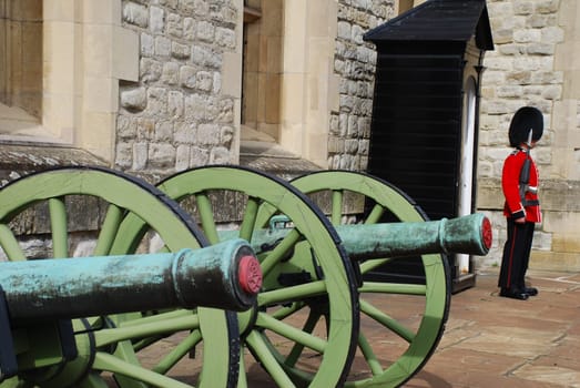 Grenadiers of the Coldstream Guard guard Buckingham Palace and the Tower of London with a rifle. They wear the famous bearskin hat. A soldier stands at the Jewel House. In the foreground conons on pivot mounts.