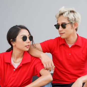 Young asian couple in red T-shirt with collar and black sunglasses looking at each other. Portrait on gray background.