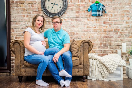 Beautiful pregnant woman and man sitting near brick wall