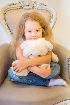 Cute girl in casual clothes sitting in the armchair and hugging toy