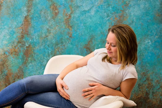 Young pregnant woman sitting on the armchair and holding her tummy