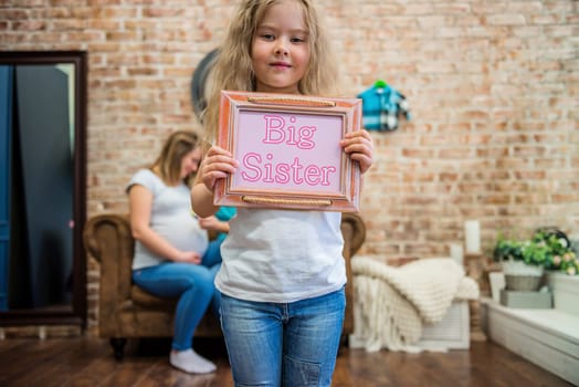 Cute girl in casual clothes standing and holding a sign with text, blurred family on the background