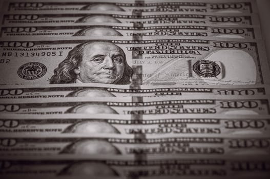 One hundred dollar bills are in a row, one stands out, selective focus. Style black and white.