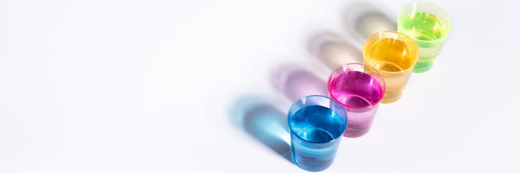 Plastic multi-colored glasses with liquid on a white background with highlights. Layout, mockup.