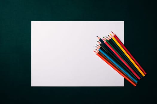 A blank white sheet and colored pencils for drawing on a plain textured background with space for copying and lettering. Layout, mockup free space.