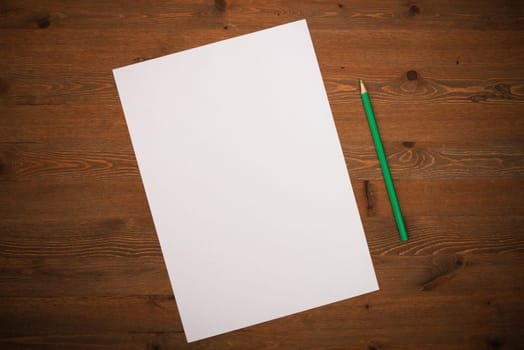 A blank white sheet and pencil for drawing on a wooden background with space for copying and lettering. Layout, mockup free space.