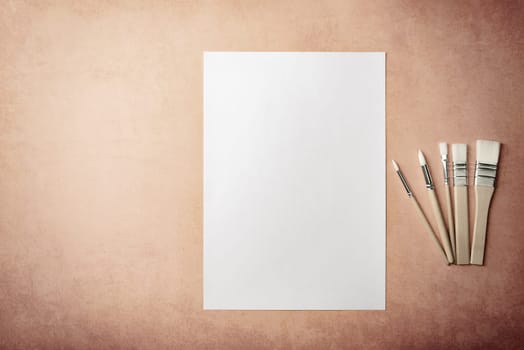A clean white sheet and brushes on a textured background with space to copy. Layout, mockup space for text and drawing.