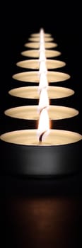 A row of burning candles on a dark background with a flare in the foreground. Layout, mockup.